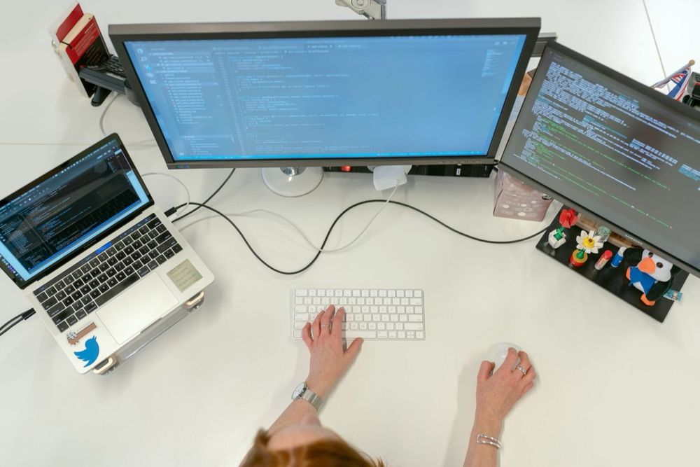 A developer writing code at dual monitors on a clean white desk