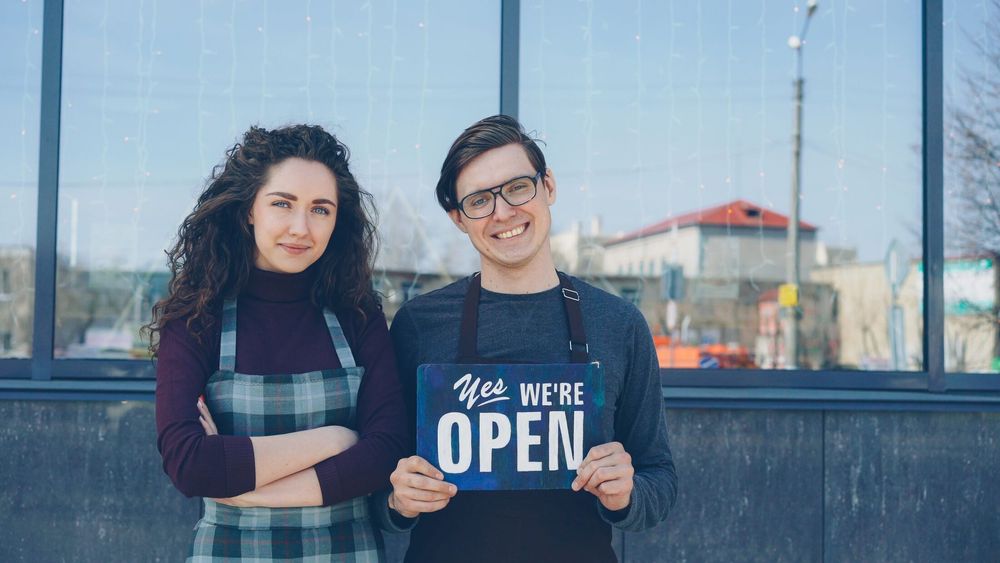 Two independent shop owners holding an open sign outside their store